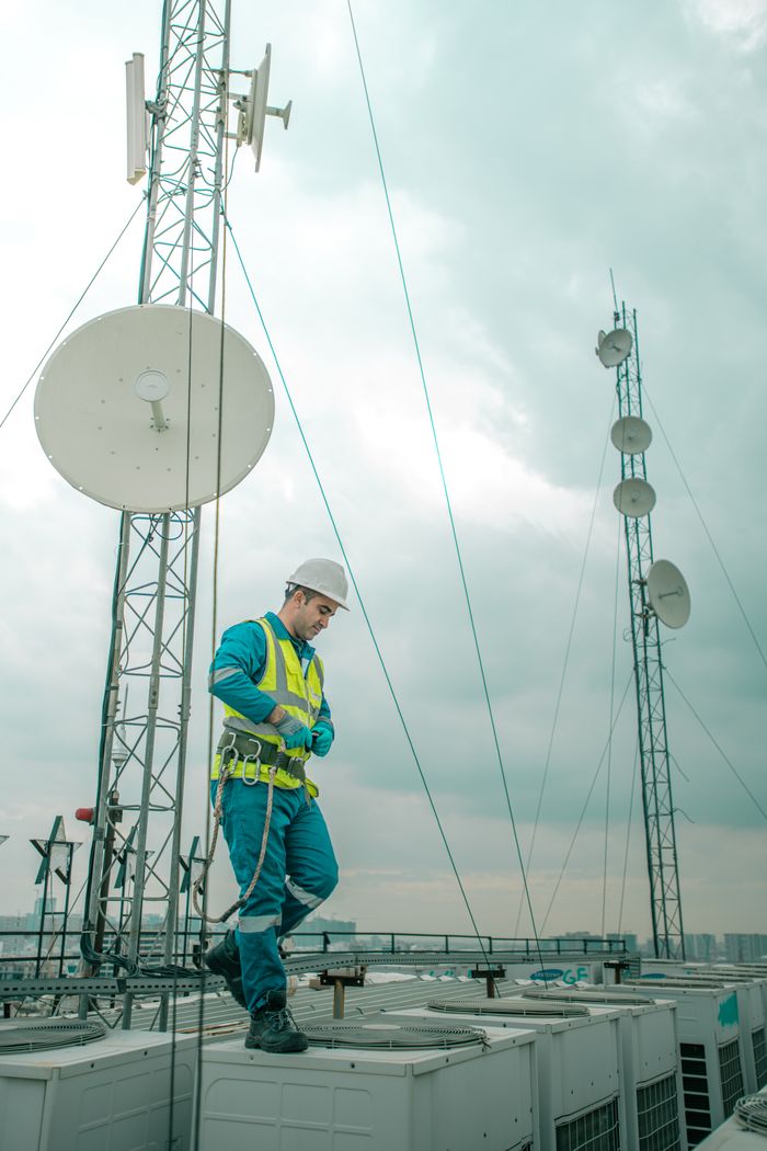 Mastering the First Impression: Your intriguing post title goes here Telecommunications worker in Shaqlawa adjusting equipment on rooftop, wearing safety gear.