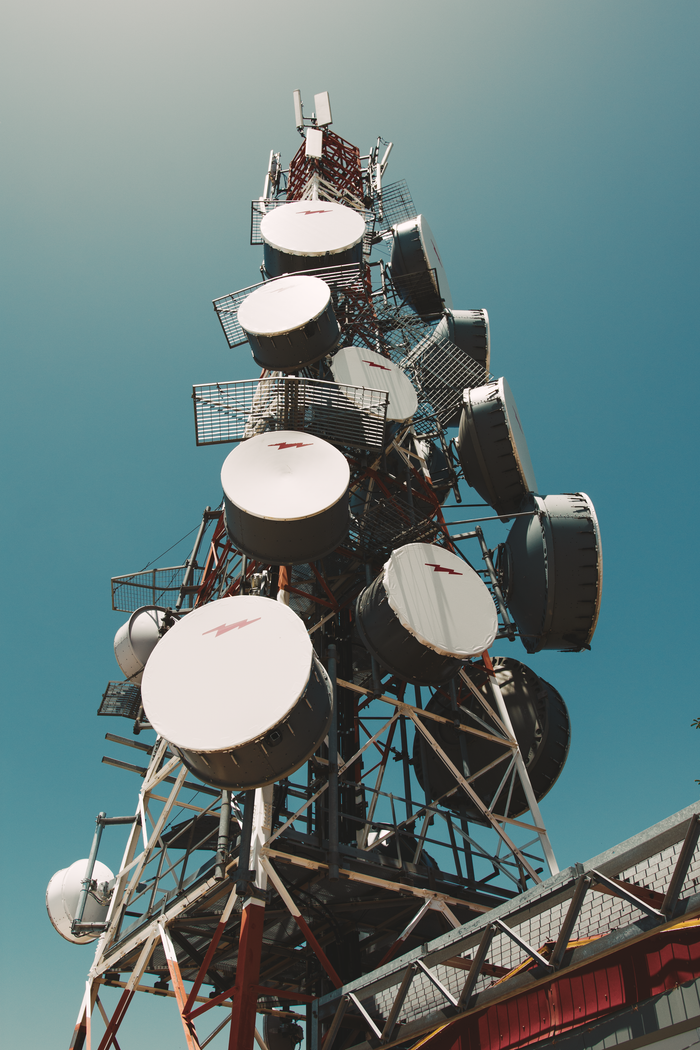 about-us-02 A towering communication tower with satellite dishes under a clear blue sky, symbolizing telecommunications.