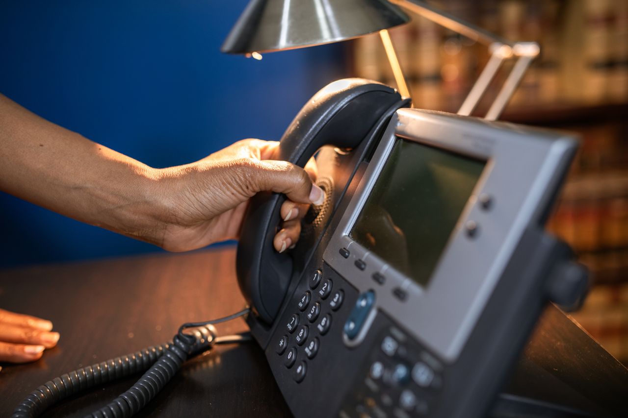 services-03 A close-up image of a hand picking up a handset from an office telephone, emphasizing communication device usage.