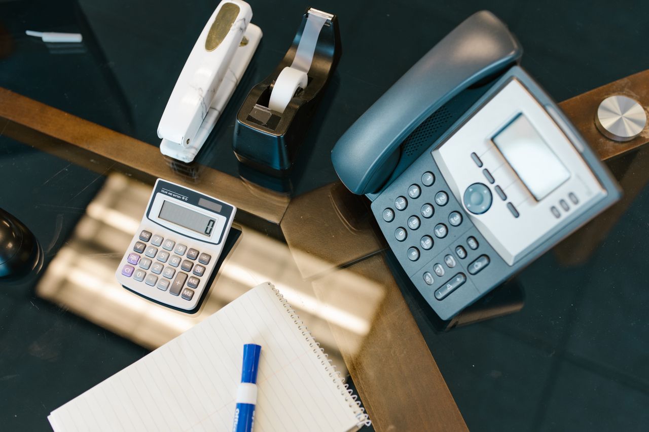 services-04 A neatly arranged office desk with a calculator, phone, stapler, tape, and notepad.